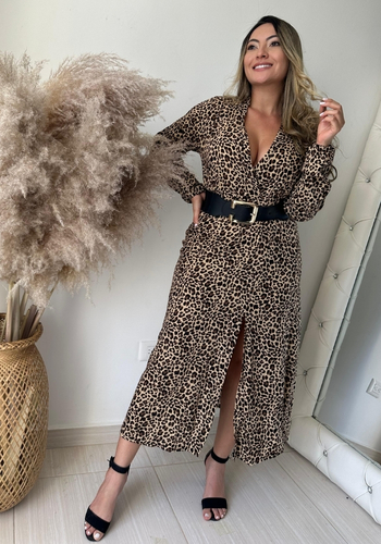 Mujer posando con un vestido de estampado de leopardo y cinturón negro, frente a una planta decorativa grande.