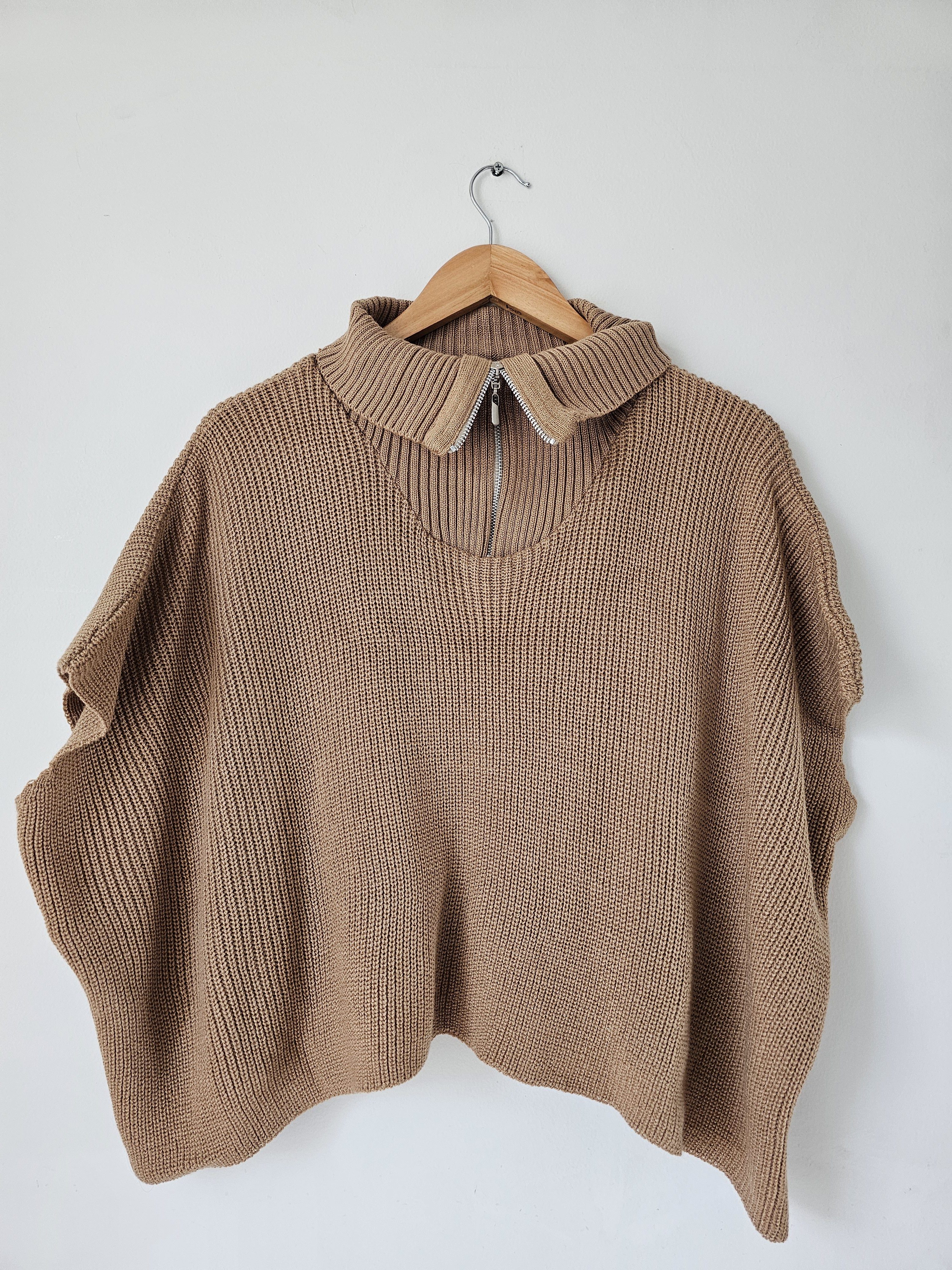 Ruana o poncho tejido para mujer en color camel con cremallera plateada en el cuello. Capa de silueta amplia y mangas cortas caídas. Prenda de hilo estilo casual y moderno. Talla Única. Jessi Boutique.